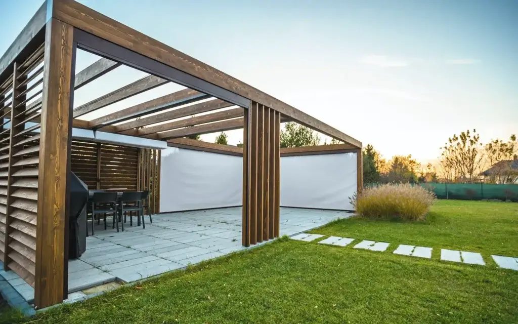 Timber pergola with a dining area and light-coloured side screens, opening onto the garden.