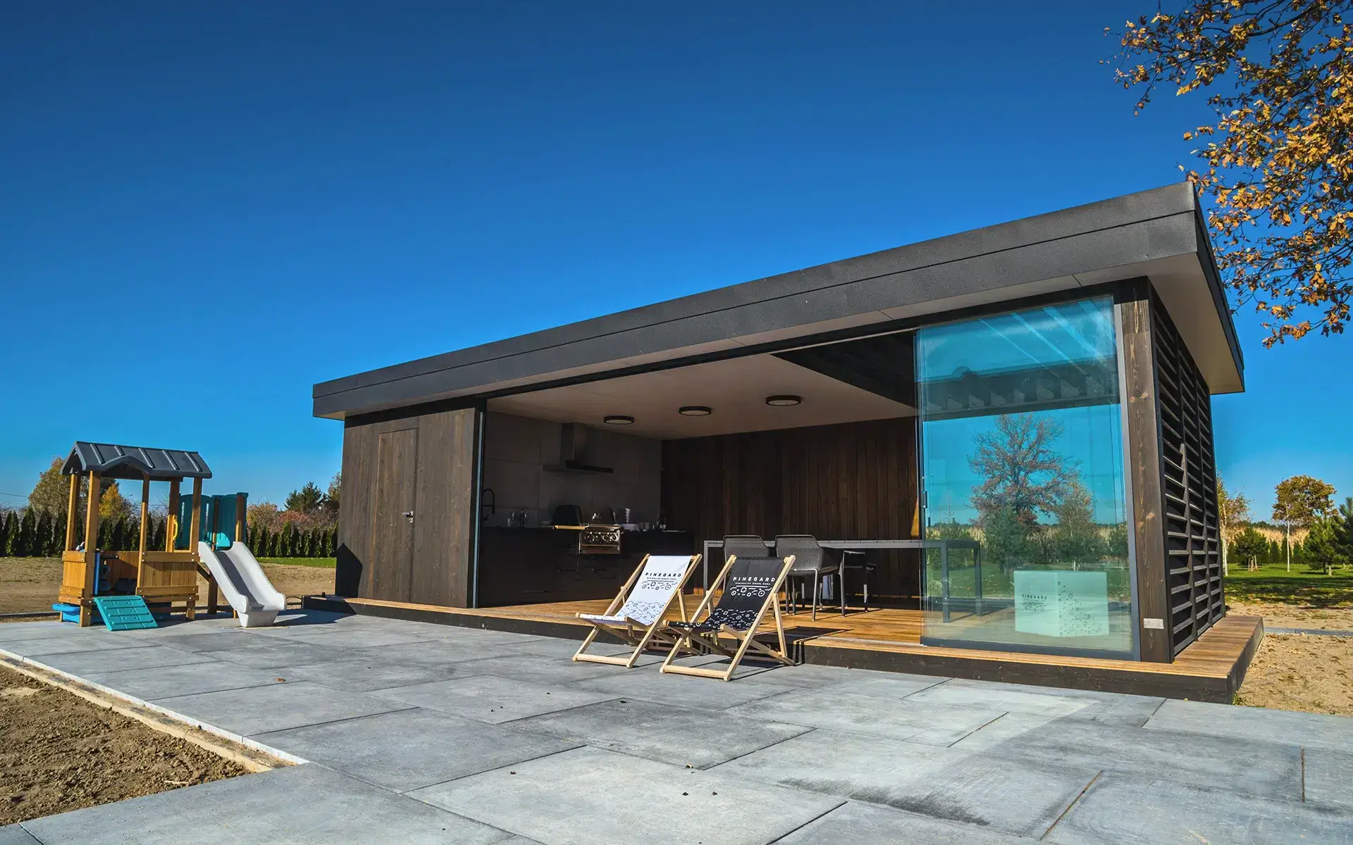 Pinegard garden room with extensive glazing, a kitchen and terrace seating.