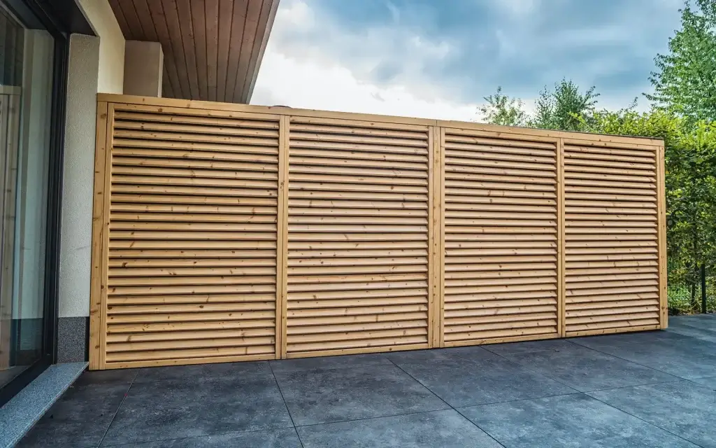 Auf dem Bild sieht man einen langen Sichtschutz aus Holz neben einem Haus. Der Sichtschutz besteht aus mehreren Holzelementen.